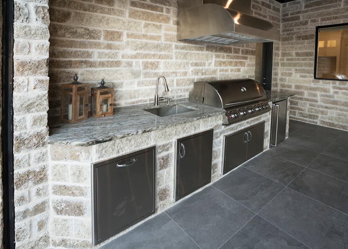 Covered outdoor kitchen with granite counters, grill, sink, and stone cabinetry