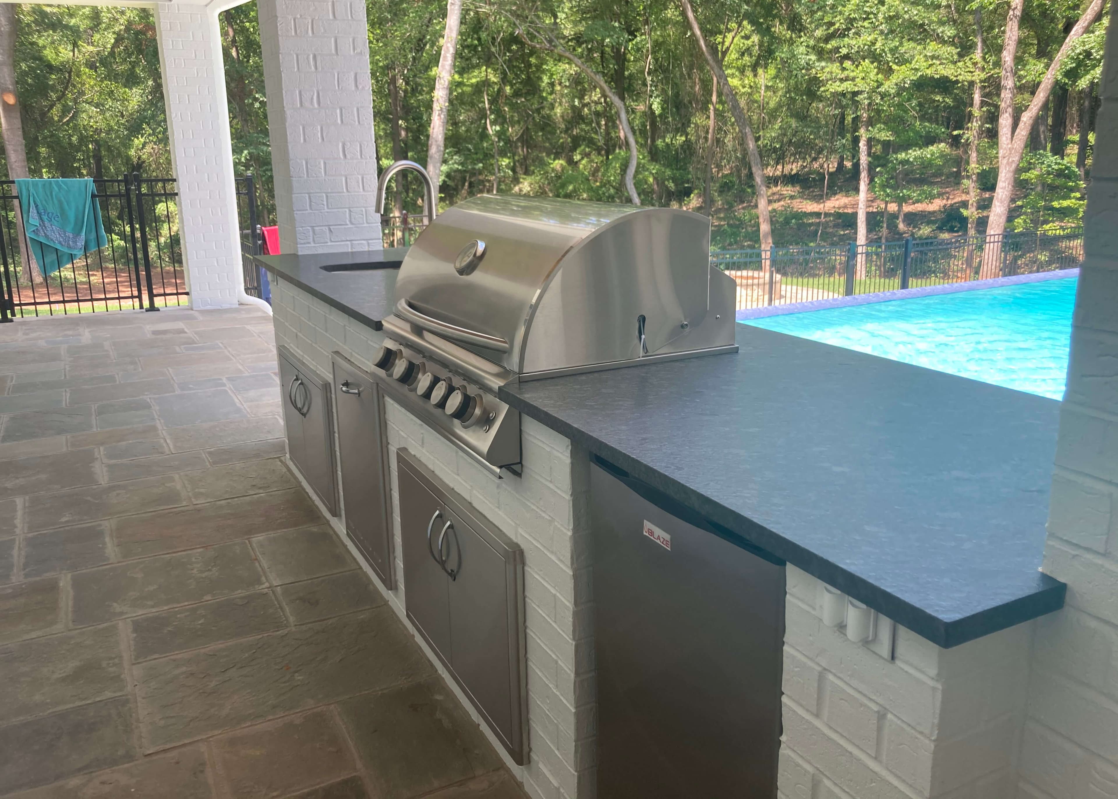 Covered outdoor kitchen beside a pool with dark stone counters