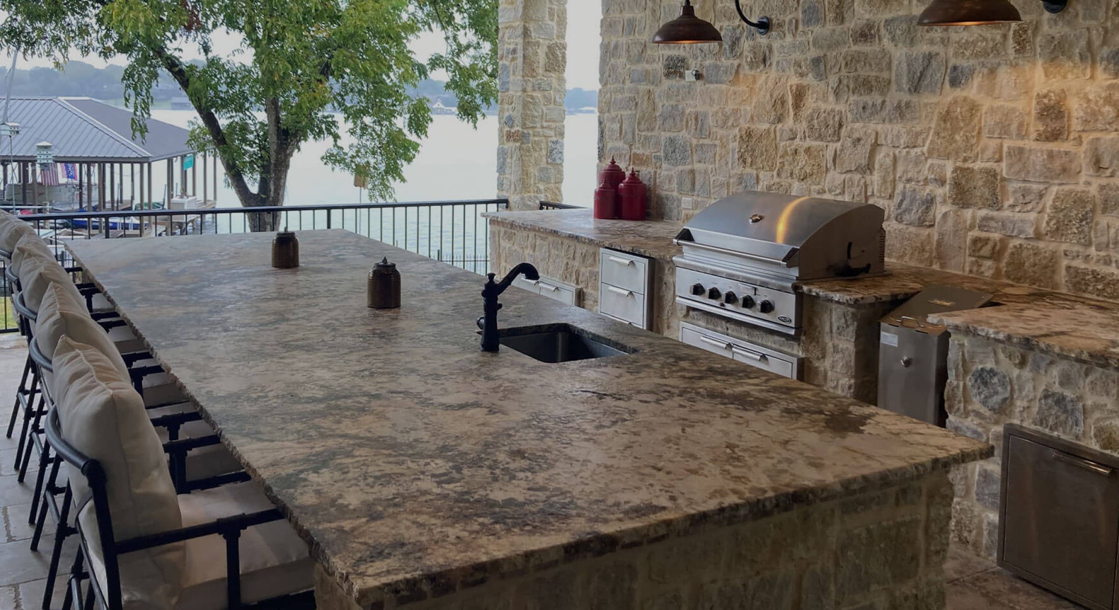 Finished outdoor kitchen with stone counters, a grill, sink, and lake view